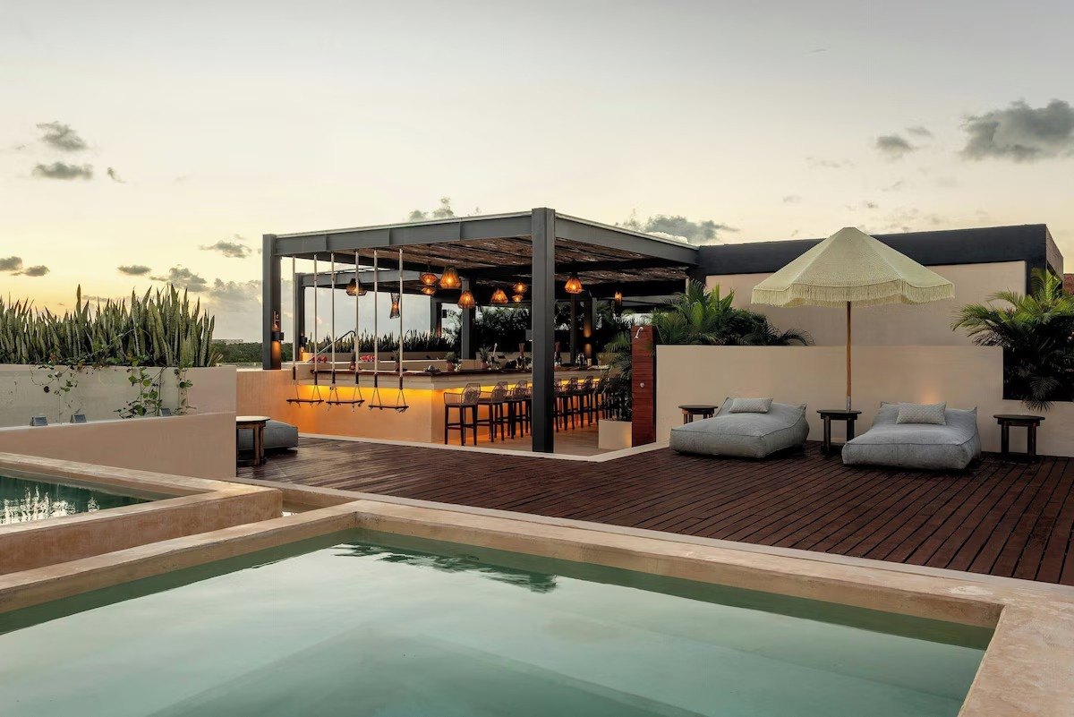 Rooftop al atardecer con alberca, camastros y bar bajo pérgola