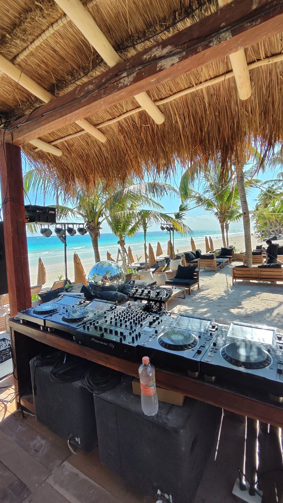 DJ equipment in the booth with the beach and lighting behind