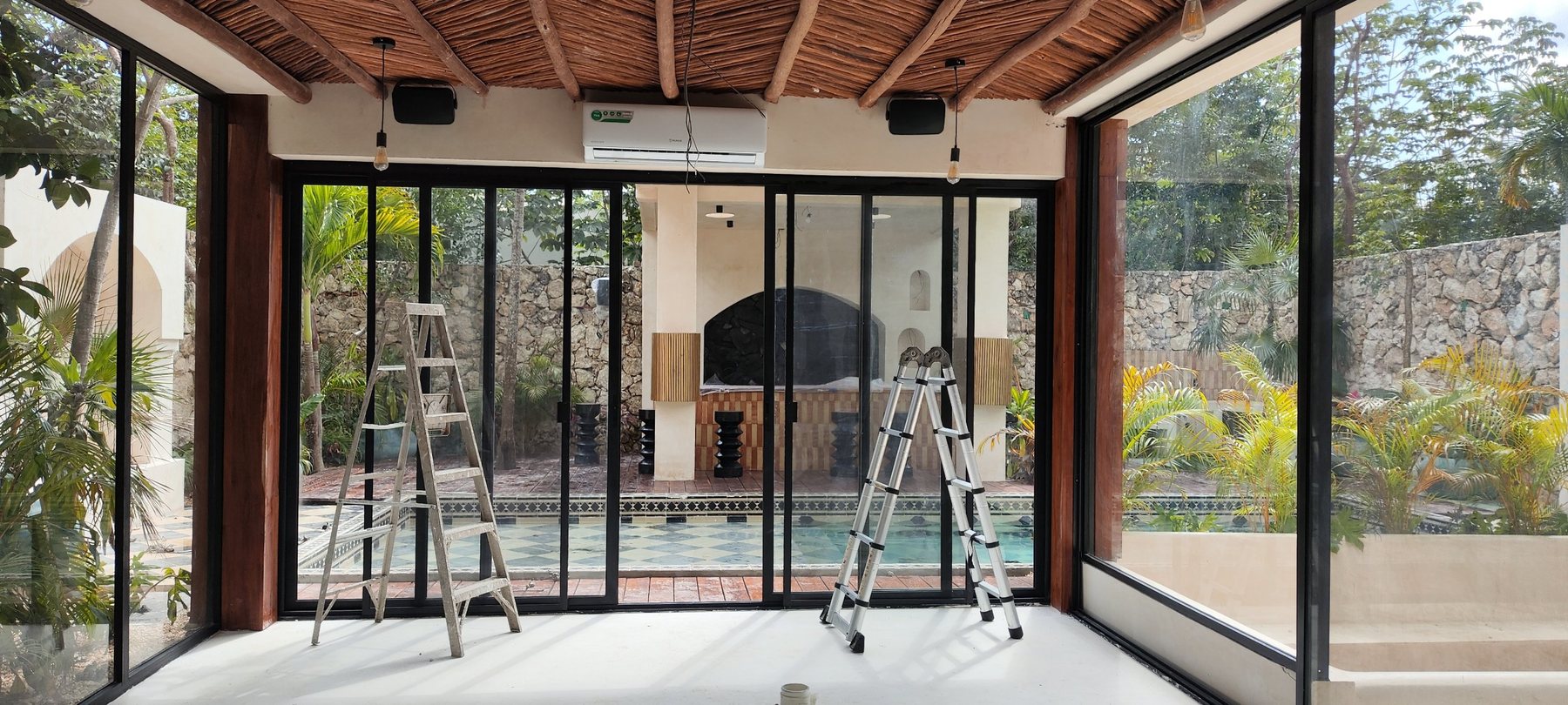 Glazed room with black JBL loudspeakers by the ceiling, facing the pool